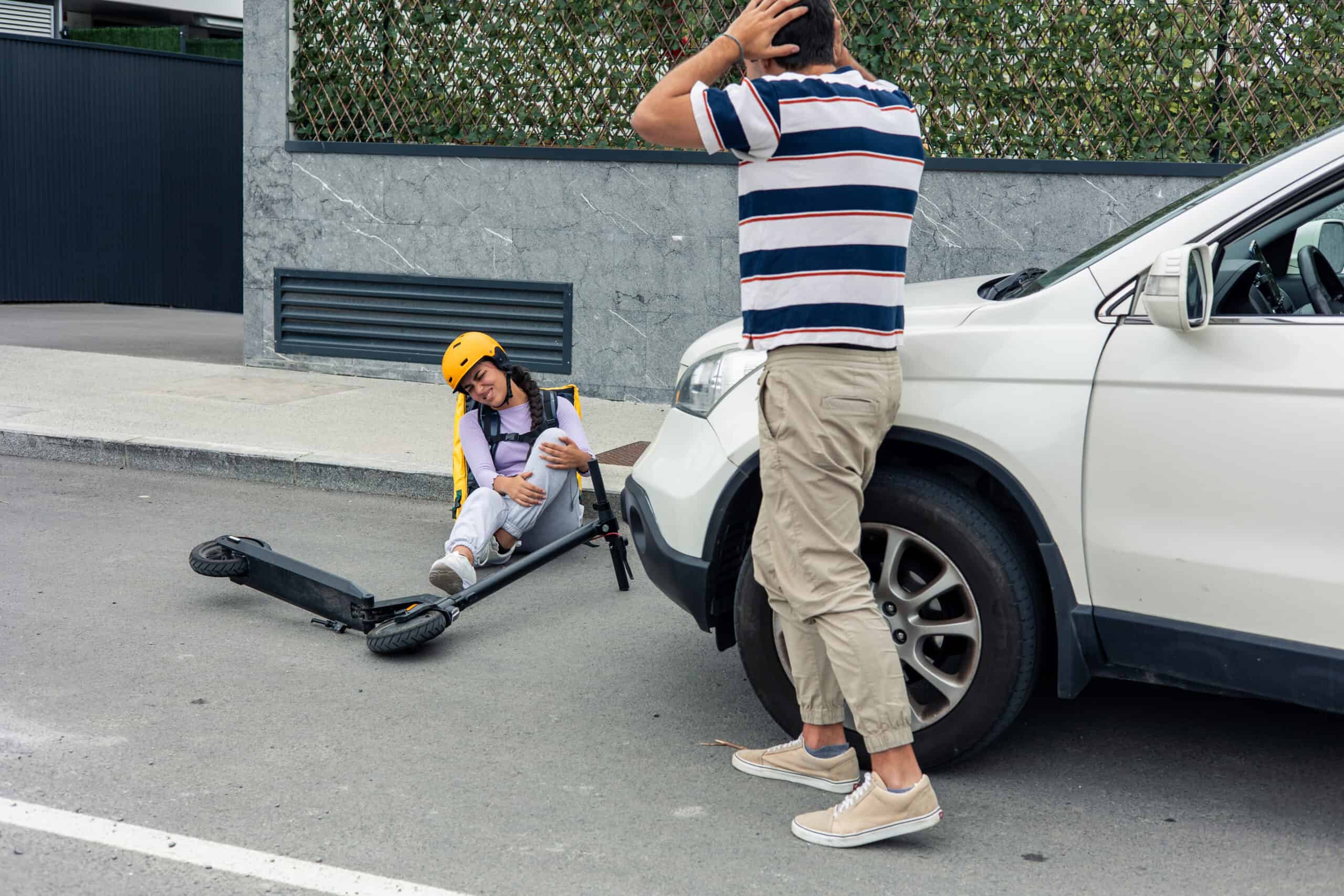 scooter accident. woman in pain on the ground with her scooter. man next to car, worried about woman