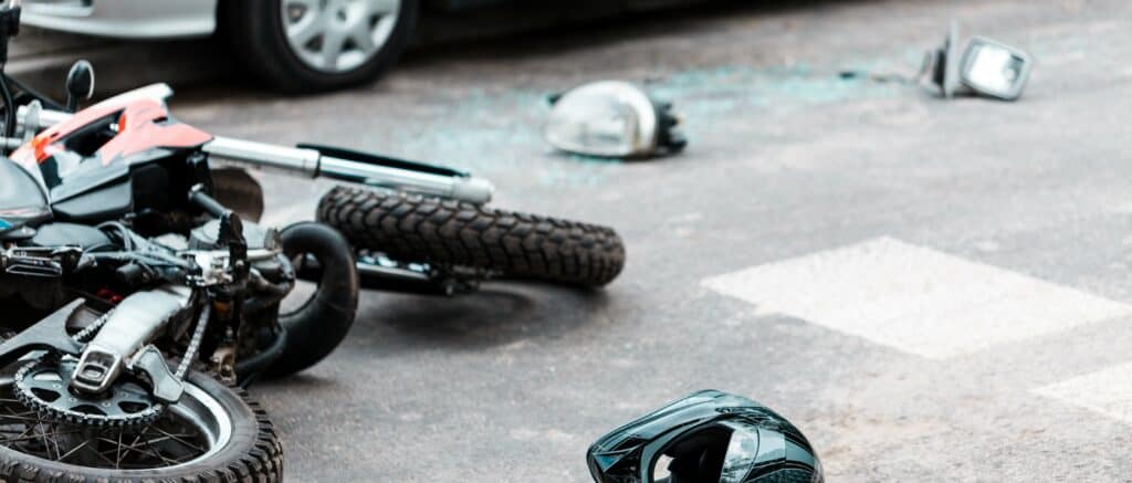 Motorcycle crash in a crosswalk with broken glass on the ground.