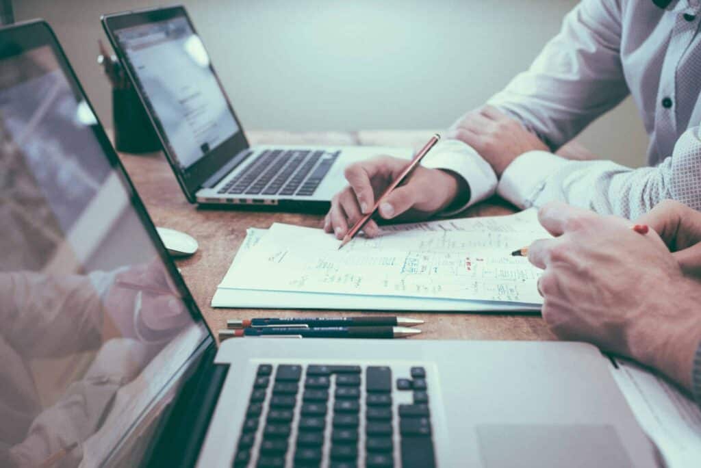 dos personas a una mesa con ordenadores y papeles