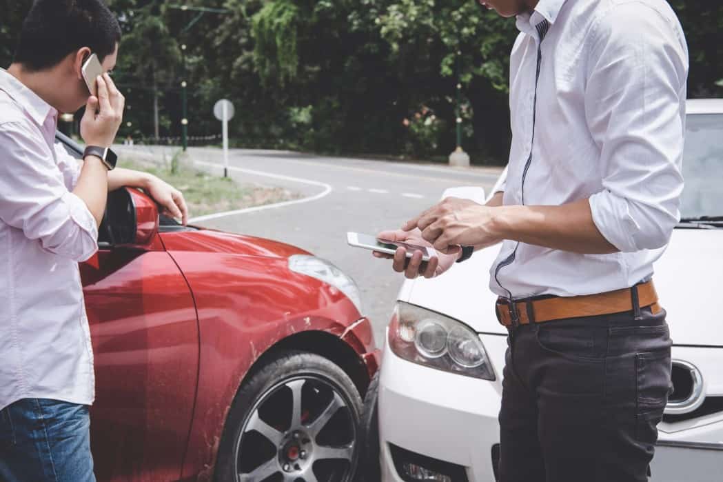 Two drivers arguing after a car accident and making a phone call to insurance.