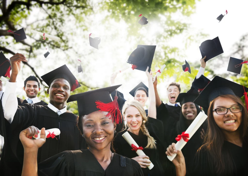 Happy graduate. Low angle view of happy young African man in graduation gown holding his mortar board against blue sky