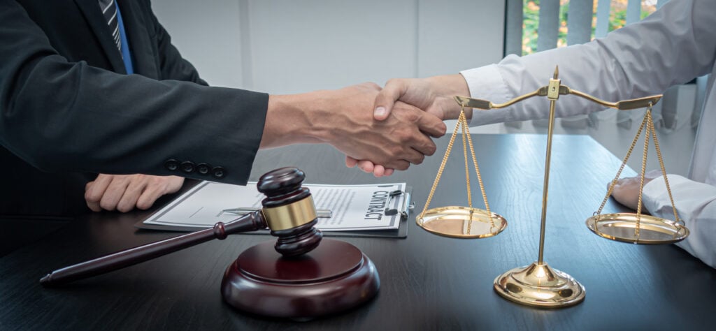 two people wearing suits shaking hands over a desk after a case result