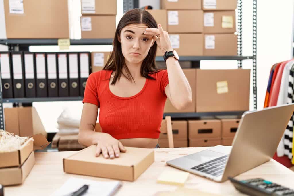 A concerned woman in a red shirt sitting at a desk with a closed package, indicating uncertainty about the contents of an online order.