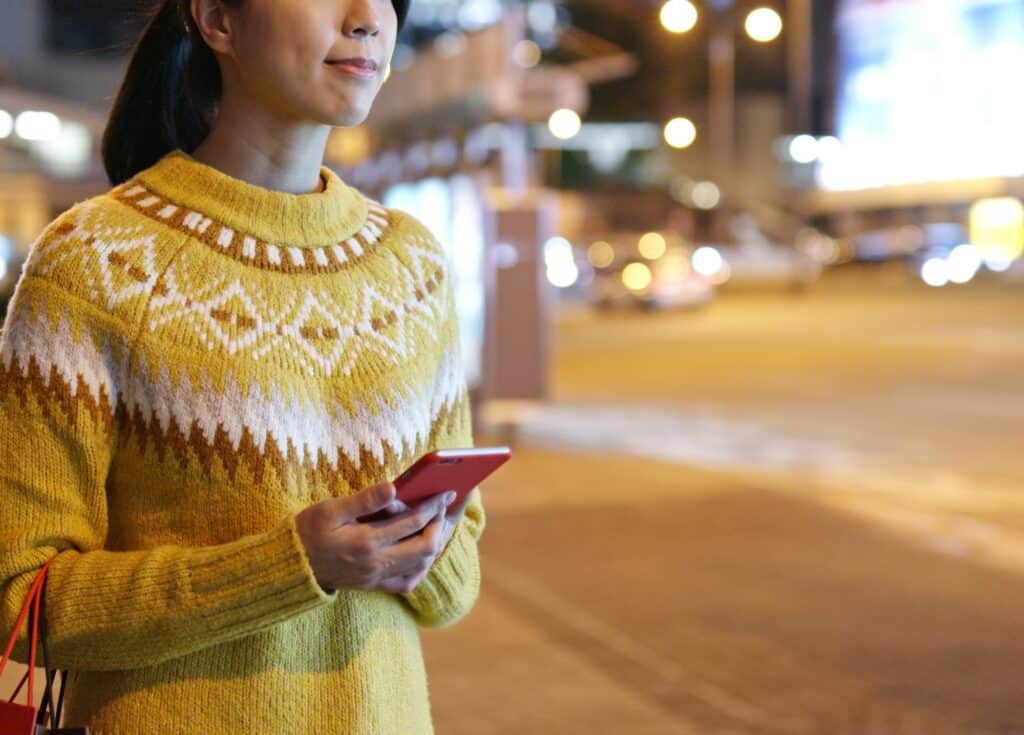 Mujer sujeta el teléfono con la app de Uber mientras espera un vehículo.