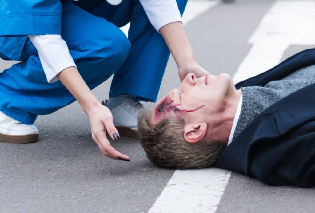 Hombre accidentado con lesiones faciales está tumbado en la calle.