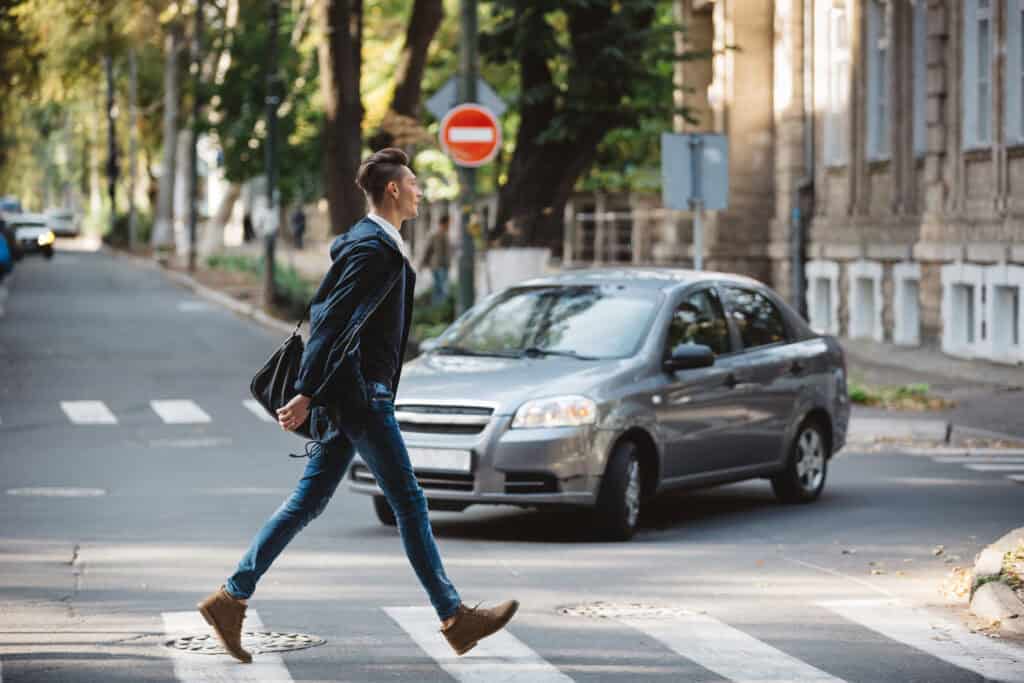 Hombre cruzando la calle en un paso peatonal con un vehículo acercándose.
