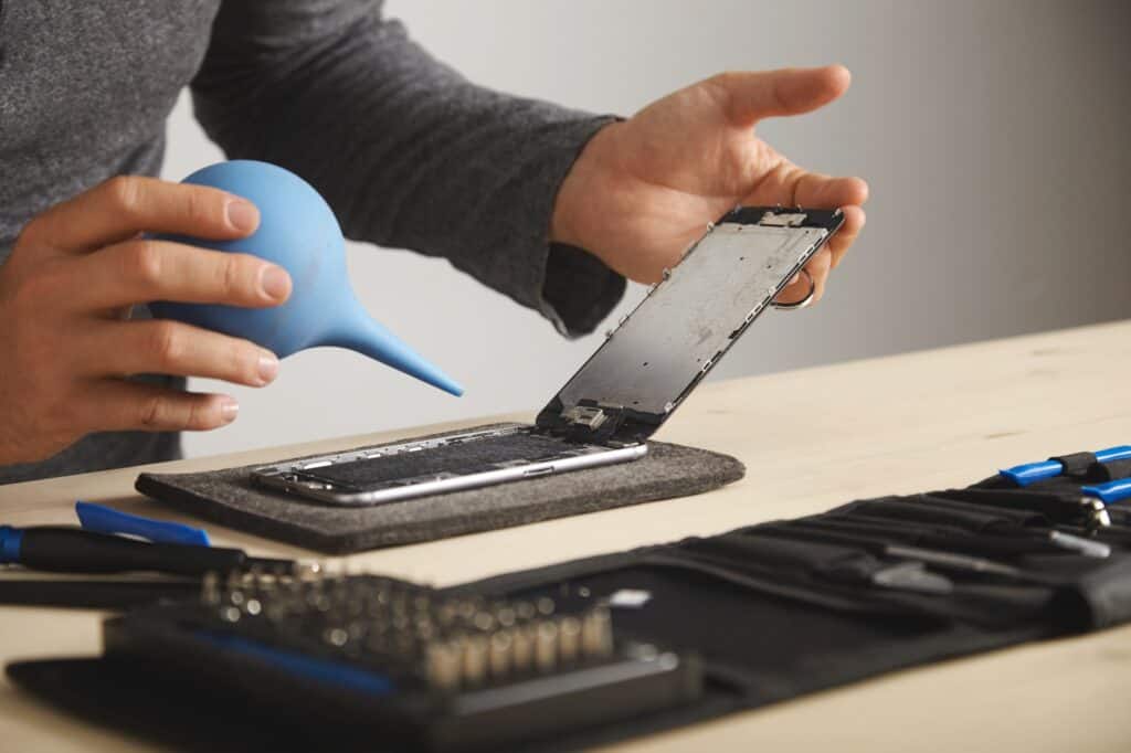 A person cleaning the inside of a disassembled smartphone.