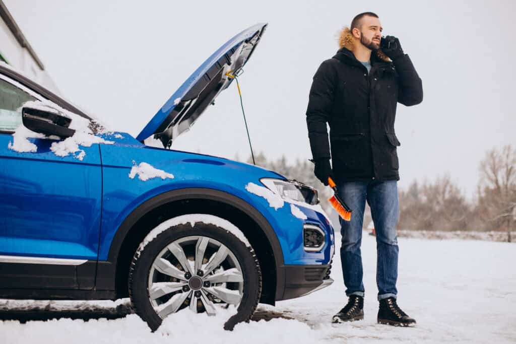 Un hombre pide ayuda junto a un vehículo azul cubierto de nieve.