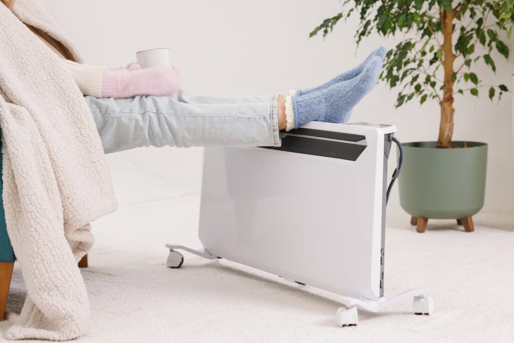 Young girl in warm knitted socks warms her feet on a space heater