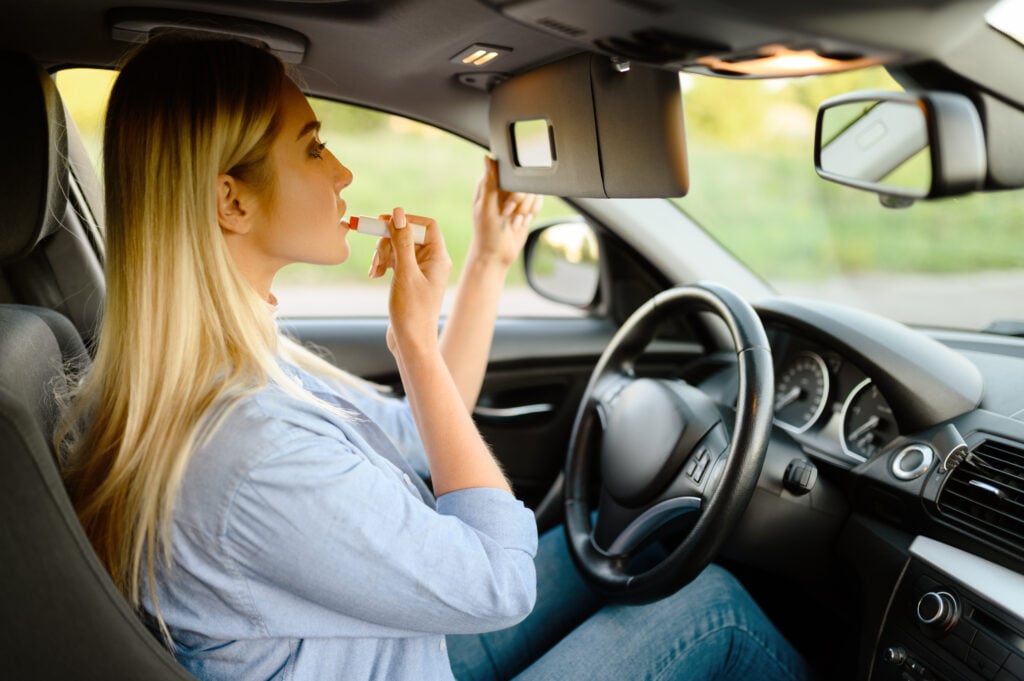 Woman applying makeup in her car, demonstrating that distracted driving is a common habit.