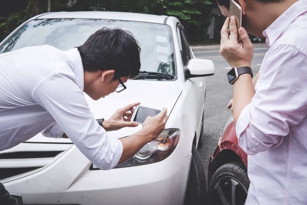 Two drivers arguing after a car accident and making a phone call to insurance.