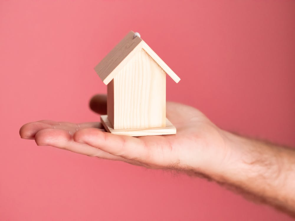 A homeowner holding a wooden house model representing insurance coverage.