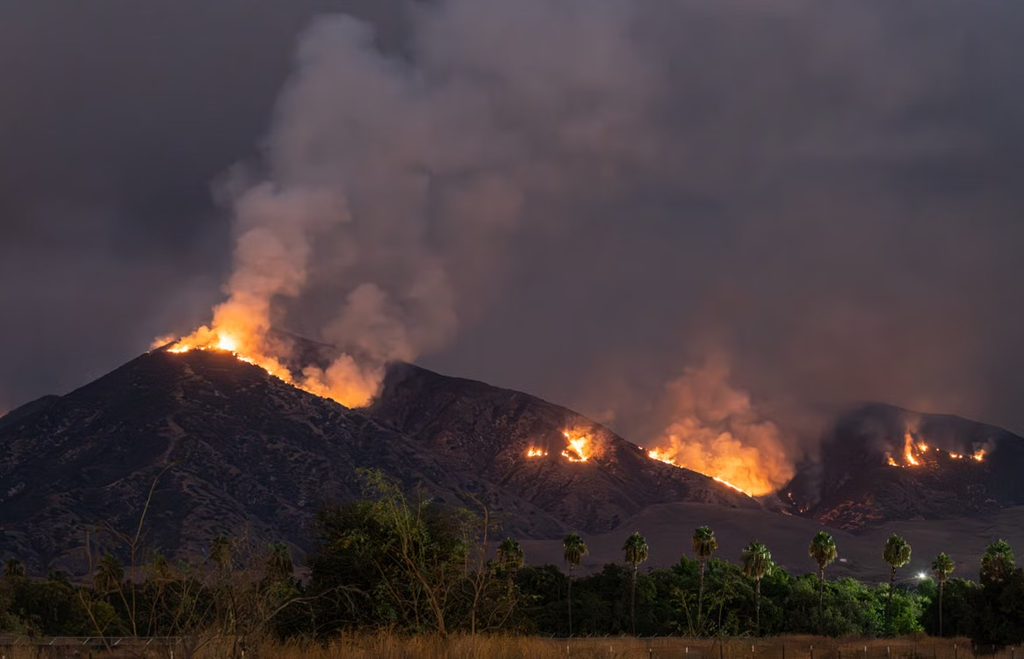 A nighttime view of a California wildfire, with intense flames and an orange glow from the fire.
